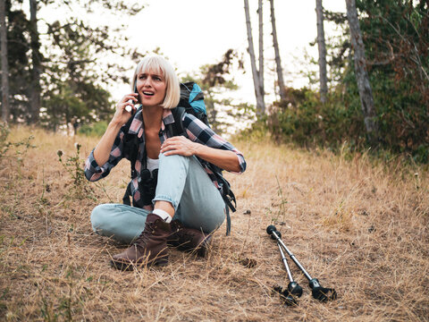 Woman hiker experiencing knee pain while hiking in the forest, using her phone to call for help and rescue assistance.