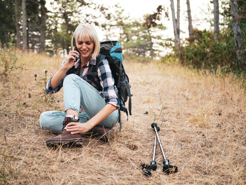 Woman hiker calling for emergency assistance on her mobile phone while dealing with ankle pain and leg injury in the forest.