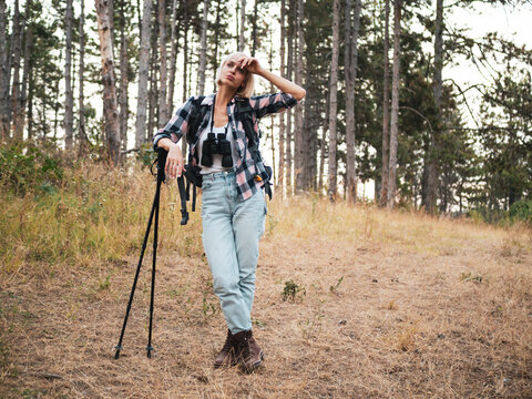 Tired woman hiker resting in the wilderness after hiking, carrying backpack and hiking pole while taking a break from walking through the forest.