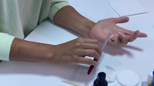 A woman carefully files her fingernails at a white desk. She shapes them with patient focus and gentle care. This quiet self care routine feels peaceful and satisfying.