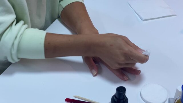 A woman gently wipes her fingers with a cotton pad at a white table. She cleans her nails during a calm manicure session. This peaceful moment feels satisfying and refreshing.