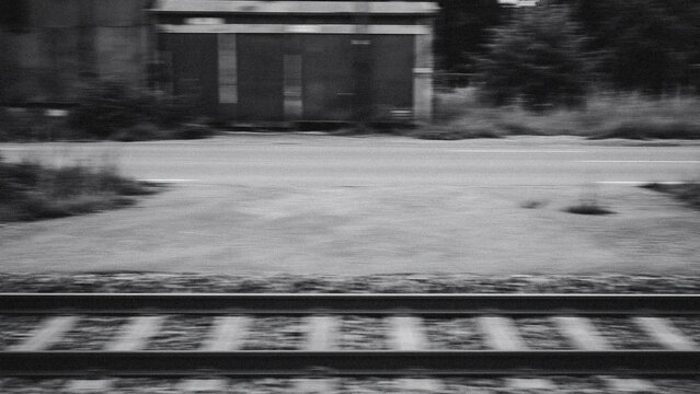Blurred black and white train tracks with industrial building in background in outdoor setting with copy space