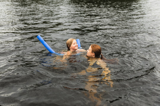 Mother and young girl floating with pool noodle in lake