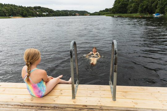 Mother swimming on back while daughter watches from pier