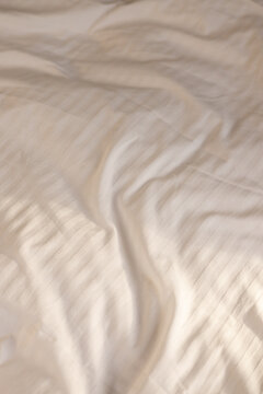 Rumpled White Striped Bedsheets with Warm Morning Sunlight and Shadows