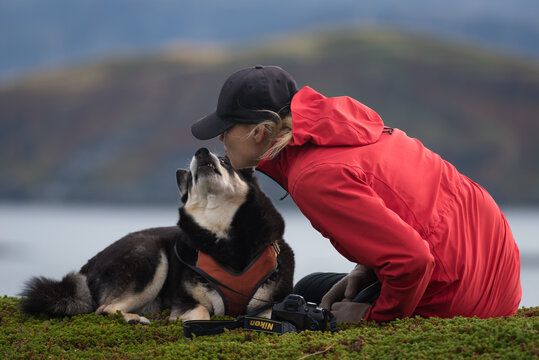 Woman in red jacket and dog overlooking rocky shore