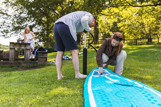 Couple inflating stand up paddleboard with manual pump on grass