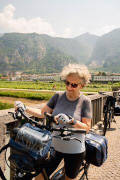 Senior woman cyclist checking phone by Adige River in Italy