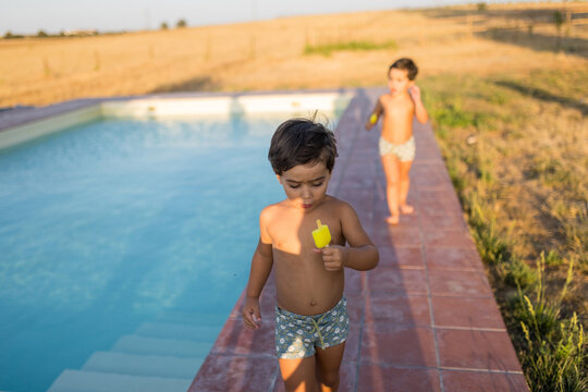 Boy eating ice cream while walking by pool during summer vacation