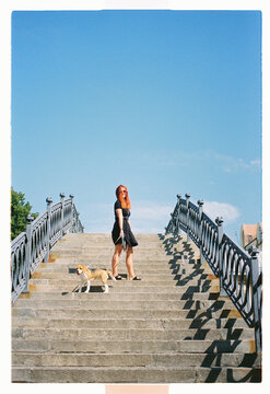 A red-haired woman and her beagle pause on grand stone steps
