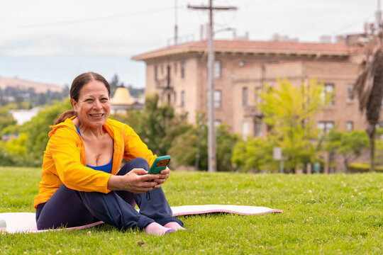 mature woman smiling holding cellphone sitting on exercise mat