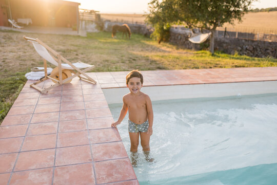 Boy standing in swimming pool at country house on summer evening