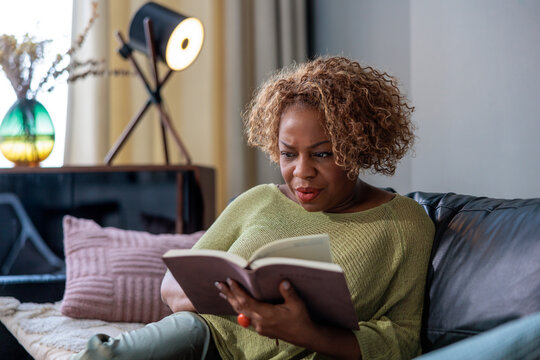 A woman relaxing on a sofa, engrossed in a book