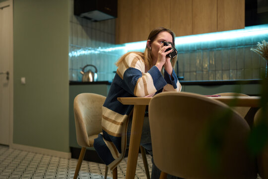 Female seated at kitchen table drinking from mug in modern interior