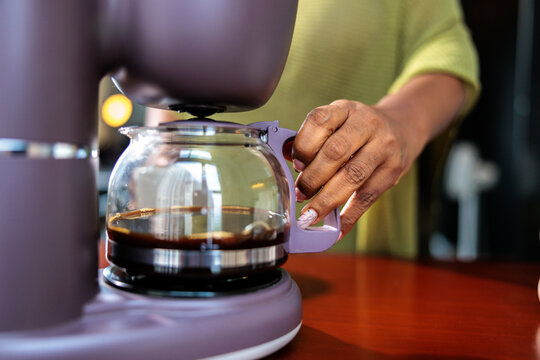 A hand removing a carafe from a coffee maker