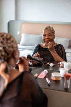 Mature woman applying lipstick in front of a vanity mirror