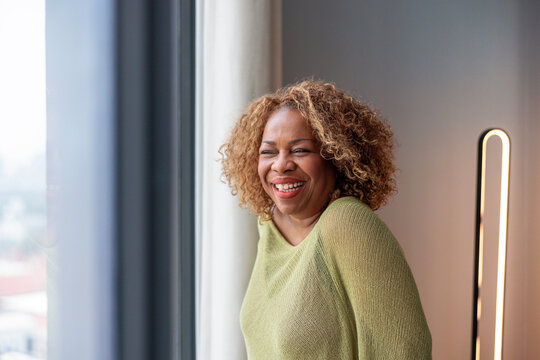 A joyful woman smiling near a bright window