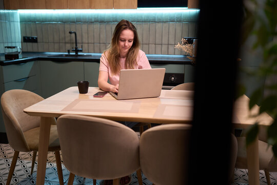 Freelance woman typing on laptop at table in contemporary kitchen