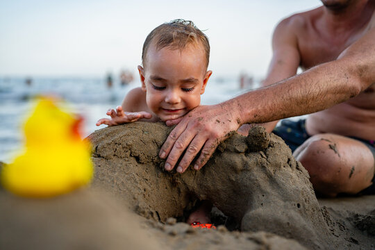 Baby boy playing with father building sandcastle on beach