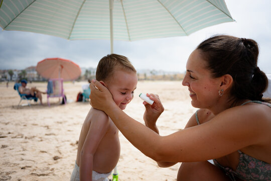 Mother applying sunscreen stick to son on beach