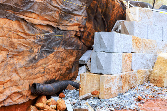 Workers are using blocks retaining wall with drainage pipe tubing at construction site located