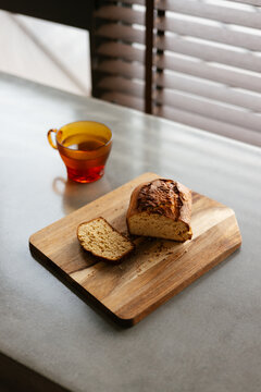 Artisanal Loaf Cake on Wooden Cutting Board beside Amber Glass Tea Mug
