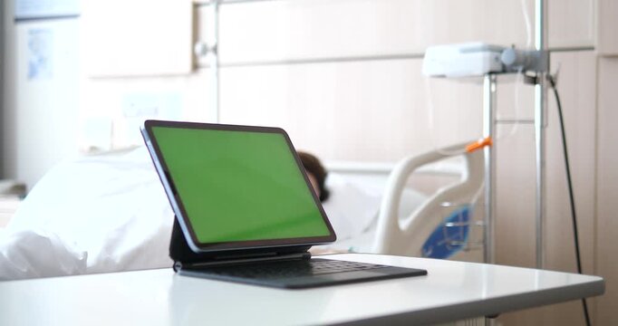 Green screen tablet mock up on overbed table with blurred patient on hospital bed