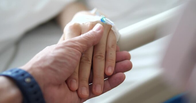 Close up of holding patient hand with IV saline solution in hospital