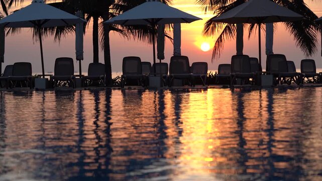 Captivating Sunset Reflections by the Tranquil Poolside: A Serene Moment of Nature's Beauty with Silhouettes of Palm Trees and Lounge Chairs