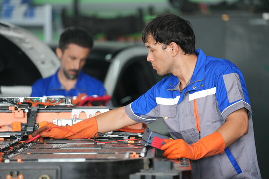 EV Technician Testing High Voltage Electric Vehicle Battery Pack with Multimeter in Repair Workshop