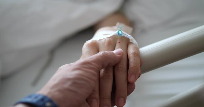 Close up of holding patient hand with IV saline solution in hospital