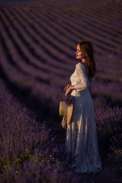 Woman lavender field romantic sunset portrait in beautiful white dress holding straw hat