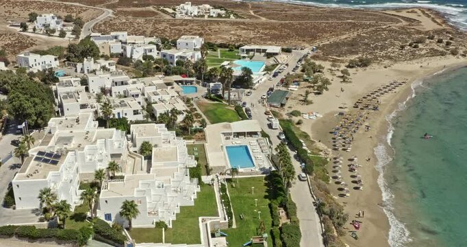 Chrisi Akti Paros Greece Aerial v2 birds eye view fly around hillside beach resorts capturing beautiful summer landscape with rows of sunbathers relaxing on the sandy beach - September 2021