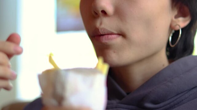A vibrant teenage girl eats French fries while sitting in a fast-food cafe, offering an authentic lifestyle scene filled with appetite, comfort, and youthful charm. Mouth close-up.