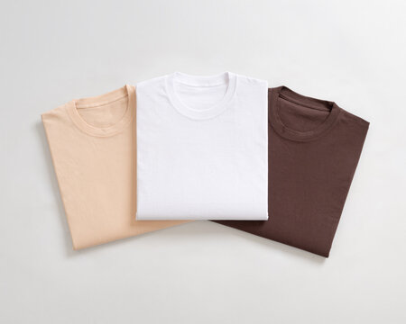 Three neatly folded cotton t-shirts in earth tone colors arranged on a clean white background for catalog display