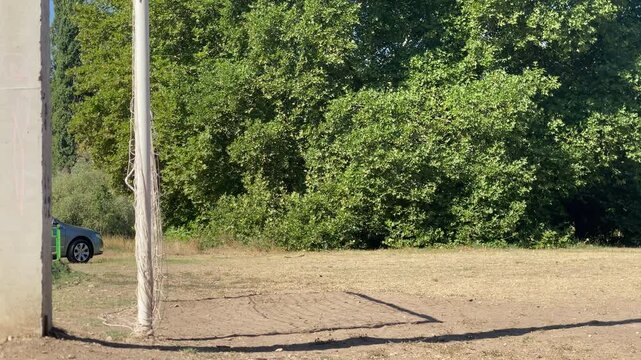 An empty soccer goal stands quietly on a dry dirt field. Lush green trees surround the park, creating a serene and peaceful atmosphere.