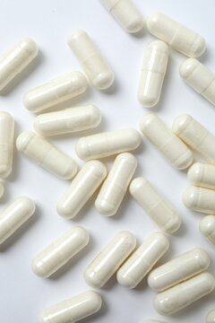 White capsules scattered on white surface, top view. Clean and minimalist medical background