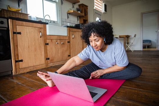 Woman stretching on yoga mat with laptop in kitchen