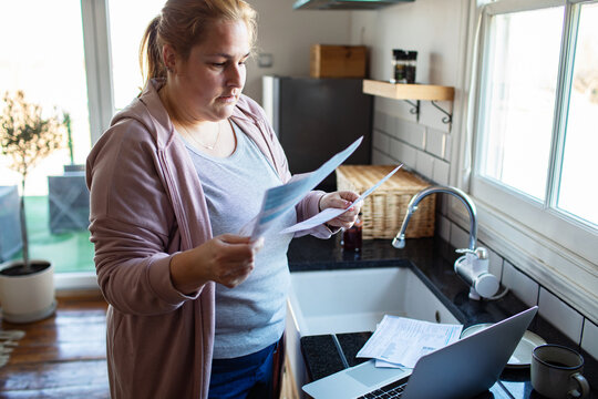 Woman reviewing bills with laptop in kitchen