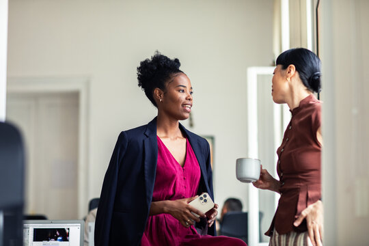Two coworkers chatting by office window during coffee break