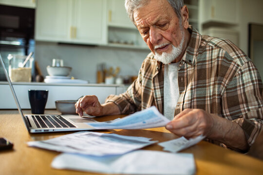 Senior man paying bills with laptop at kitchen table