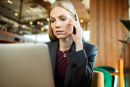 Concerned businesswoman touching temple while working on laptop