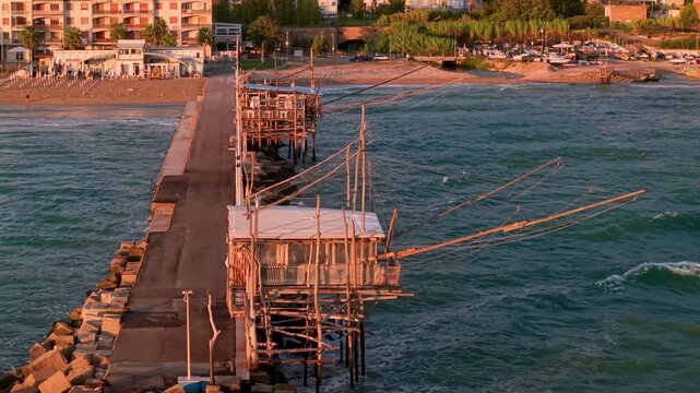 Marina di San Vito Chietino Trabocchi Abruzzo Italy 70mm drone golden sunrise pier two traditional trabocco restaurants with beach town view and crashing waves ambient sound 4k video