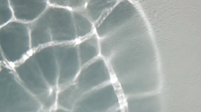 Sunlight casting caustics pattern reflections through water onto a white wall, creating a serene and abstract aquatic design texture background