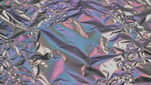 Abstract background featuring shimmering crumpled metallic foil texture with iridescent rainbow light reflections creating a modern holographic surface pattern