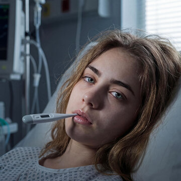 Concerned Young Female Patient Measures Her Body Temperature with a Digital Thermometer in Hospital Ward