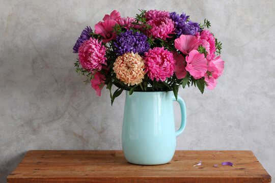 Garden flowers, asters and lavatera in a blue enamel jug, a bright autumn bouquet on the table. Cultivation, gardening, bouquet making.