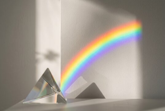 Prismatic rainbow sunlight flare on clean neutral plaster wall.