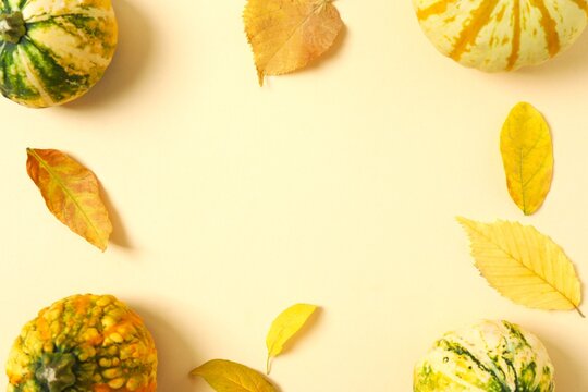 Autumn frame with decorative pumpkins and yellow leaves on beige background. Creative layout. Top view, flat lay. Design element. Halloween and Thanksgiving concept