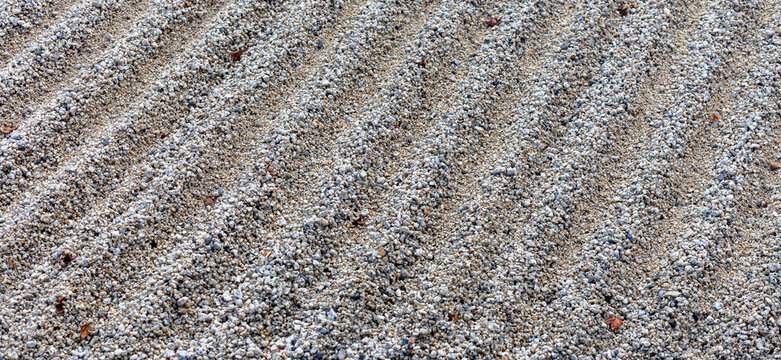 Close-up of light gray gravel arranged in parallel ridges in a traditional Japanese Zen garden, creating a textured abstract pattern associated with calm and meditation